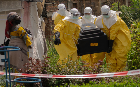 Mitarbeiter des Roten Kreuzes tragen in Schutzanzügen den Sarg einer an Ebola verstorbenen Person aus einem Gesundheitszentrum in Rwampara. - Foto: Moses Sawasawa/AP/dpa
