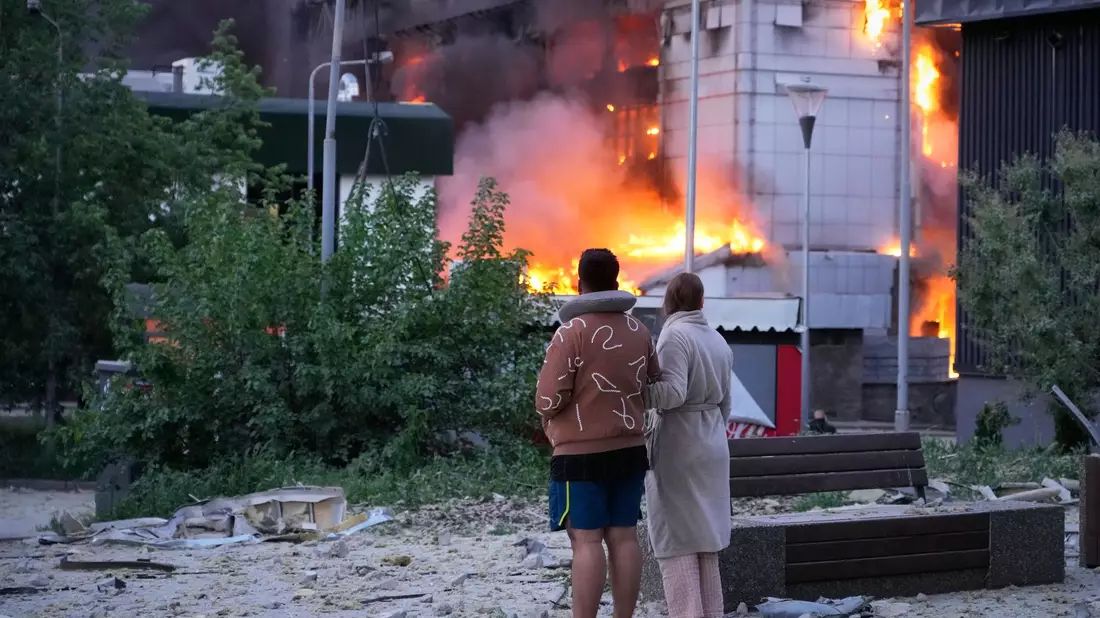 Menschen in Kiew beobachten ein brennendes Gebäude nach einem russischen Raketenangriff. - Bild: Efrem Lukatsky/AP/dpa
