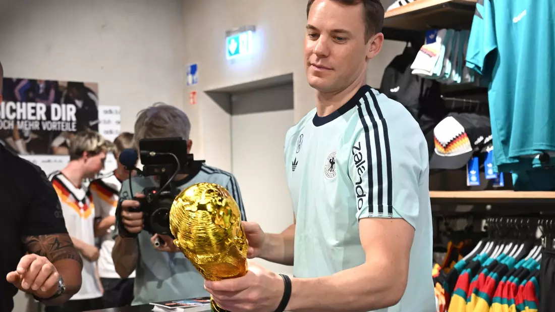 Lächelnd signiert Manuel Neuer einen goldenen WM-Pokal.  - Bild: Federico Gambarini/dpa