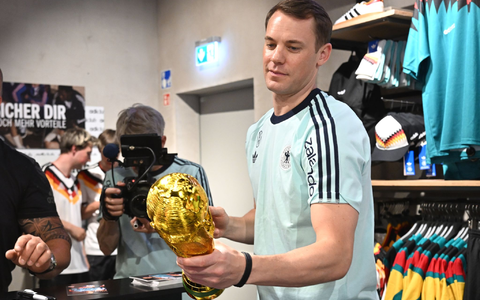 Lächelnd signiert Manuel Neuer einen goldenen WM-Pokal.  - Foto: Federico Gambarini/dpa