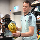 Lächelnd signiert Manuel Neuer einen goldenen WM-Pokal.  - Foto: Federico Gambarini/dpa