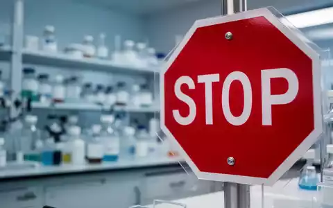 Ein rotes Stoppschild im Vordergrund, vor einem verschwommenen pharmazeutischen Laborhintergrund. - Foto: über boerse-global.de