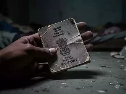 A close-up of a crumpled Indian passport in a hand, resting on a dark, cold surface, symbolizing labor exploitation. - Foto: über boerse-global.de