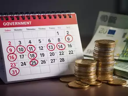 Ein Kalender mit eingekreisten Daten neben einem Stapel Euro-Münzen und -Scheinen, der finanzielle Planung und staatliche Leistungen darstellt. - Foto: über boerse-global.de
