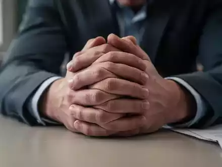 Nahaufnahme der Hände eines Lehrers, die auf einem Schreibtisch ruhen und Stress und Erschöpfung symbolisieren. - Foto: über boerse-global.de