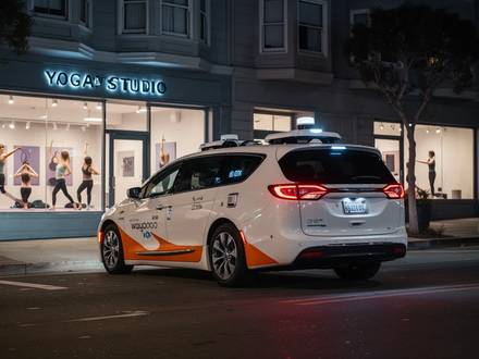 A white Waymo robotaxi with orange accents drives away from a modern yoga studio at night in San Francisco. - Foto: über boerse-global.de