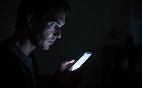 A person's silhouette in a dark room, lit by the glow of a smartphone screen, symbolizing after-hours work demands. - Foto: über boerse-global.de