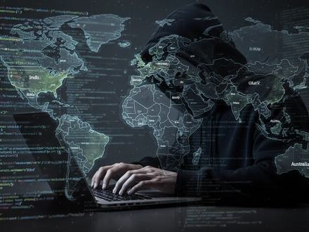 A shadowy figure in a dark hoodie typing on a laptop, surrounded by glowing code and a world map, symbolizing cybercrime. - Foto: über boerse-global.de