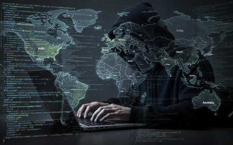 A shadowy figure in a dark hoodie typing on a laptop, surrounded by glowing code and a world map, symbolizing cybercrime. - Foto: über boerse-global.de
