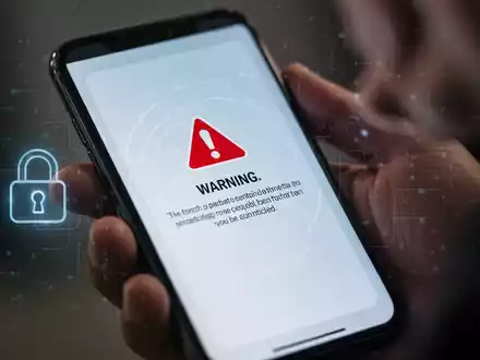 Nahaufnahme eines Smartphone-Bildschirms mit einer Warnmeldung, im Hintergrund eine Person, die das Telefon hält. - Foto: über boerse-global.de