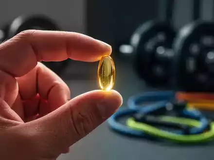 Eine Nahaufnahme einer Hand, die eine Fischölkapsel hält, mit unscharfem Hintergrund von Sportgeräten. - Foto: über boerse-global.de