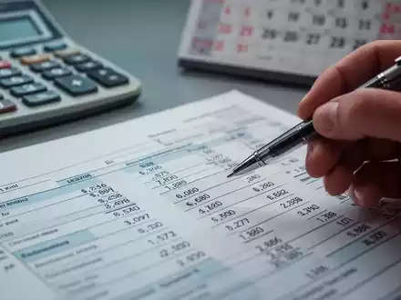 Nahaufnahme einer Hand, die mit einem Stift auf ein Steuerformular zeigt, mit einem Rechner und Kalender im unscharfen Hintergrund. - Foto: über boerse-global.de