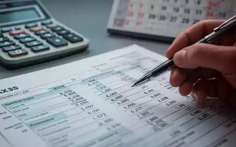 Nahaufnahme einer Hand, die mit einem Stift auf ein Steuerformular zeigt, mit einem Rechner und Kalender im unscharfen Hintergrund. - Foto: über boerse-global.de