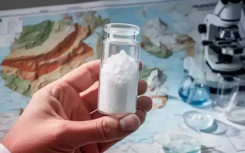 Nahaufnahme einer Hand, die ein Reagenzglas mit weißem Phosphatpulver vor einem unscharfen Hintergrund hält. - Foto: über boerse-global.de
