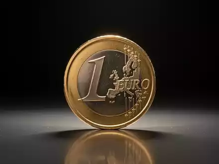 Eine einzelne goldene Euro-Münze steht auf einer reflektierenden Oberfläche, beleuchtet von weichem Licht. - Foto: über boerse-global.de