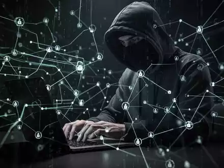 Schattige Figur in Kapuzenpullover tippt auf Laptop, umgeben von leuchtenden digitalen Linien und Netzwerk-Knoten, symbolisiert Cyberkriminalität. - Foto: über boerse-global.de