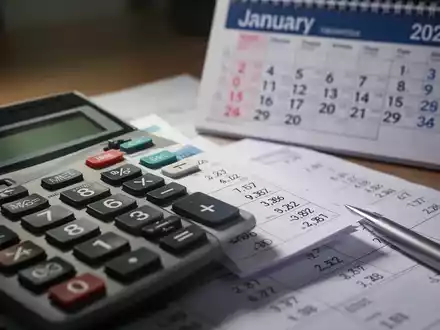 Nahaufnahme eines Taschenrechners mit Finanzzahlen und einem Kalenderblatt für Januar 2027 im Hintergrund. - Foto: über boerse-global.de