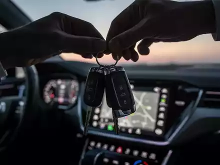 Eine Hand hält Autoschlüssel vor einem unscharfen Armaturenbrett eines modernen Autos in der Dämmerung. - Foto: über boerse-global.de