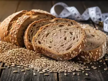 Nahaufnahme von Vollkornbrot und verschiedenen Getreidesorten auf einem Holztisch, im Hintergrund ein leicht unscharfes Maßband. - Foto: über boerse-global.de