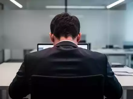 Eine Person sitzt mit gebeugtem Nacken an einem Schreibtisch vor einem Laptop, was Nacken- und Schulterverspannungen symbolisiert. - Foto: über boerse-global.de
