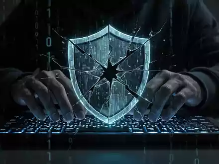 Hacker's hands on a keyboard with a broken shield icon, symbolizing a data breach at a dental insurer. - Foto: über boerse-global.de