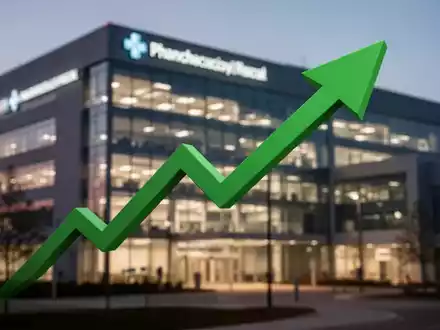 Grüner Pfeil zeigt nach oben über einem unscharfen Hintergrund einer modernen Pharma-Fassadenbeleuchtung bei Dämmerung. - Foto: über boerse-global.de
