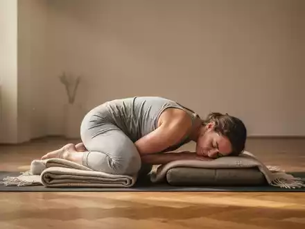 Eine Person praktiziert Restorative Yoga auf einer Matte, gestützt von Decken und Kissen in einem ruhigen Raum. - Foto: über boerse-global.de