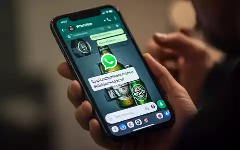 Ein Smartphone-Bildschirm zeigt eine WhatsApp-Nachricht mit einem verdächtigen Link und einem Bierlogo, während eine Hand das Telefon hält. - Foto: über boerse-global.de