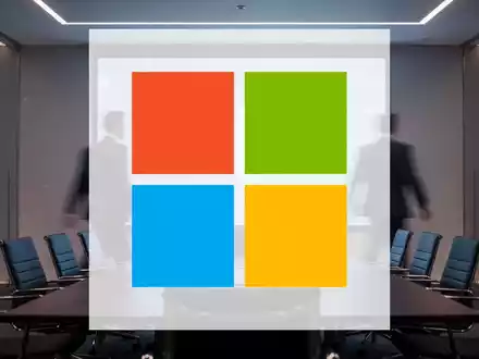 Ein Mann im Anzug geht von einem Bildschirm weg, der ein abstraktes Microsoft-Logo zeigt, in einem modernen Konferenzraum. - Foto: über boerse-global.de
