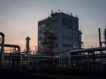 Eine Chemieanlage in Stade bei Sonnenuntergang, mit angedeuteten industriellen Strukturen und einem gedämpften Farbschema. - Foto: über boerse-global.de