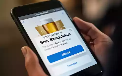 A smartphone screen showing a fake beer sweepstakes message, with a hand holding the phone. - Foto: über boerse-global.de