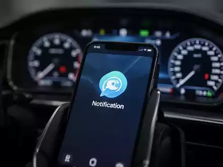 A smartphone screen showing a notification icon, with a blurred car dashboard and steering wheel in the background. - Foto: über boerse-global.de