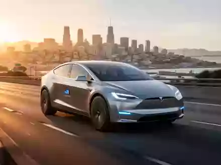 A sleek, futuristic autonomous Tesla vehicle drives on a highway with the San Francisco skyline in the background. - Foto: über boerse-global.de