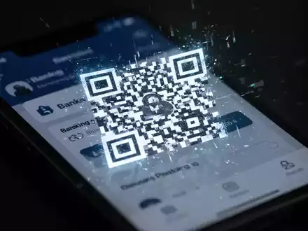 Ein fragmentierter, leuchtender QR-Code auf einem Smartphone-Bildschirm, der eine Banking-App anzeigt, symbolisiert Cyberbetrug und Quishing. - Foto: über boerse-global.de