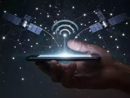 A smartphone held in a hand, with glowing lines connecting its screen to a network of satellites in a dark sky. - Foto: über boerse-global.de