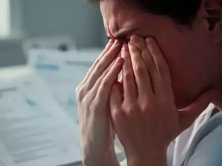 Hände einer Person, die sanft die Schläfen berühren, als Symbol für chronische Schmerzen und Erschöpfung bei Fibromyalgie. - Foto: über boerse-global.de