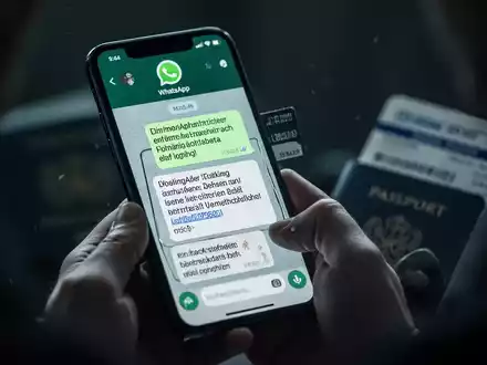 Ein Smartphone zeigt eine betrügerische WhatsApp-Nachricht mit Buchungsdetails, im Hintergrund sind Hände und Reisedokumente zu erkennen. - Foto: über boerse-global.de