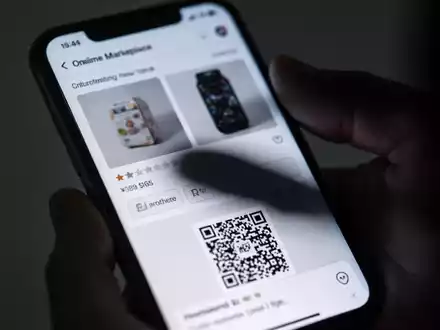Nahaufnahme eines Smartphone-Bildschirms, der eine betrügerische Online-Anzeige mit unscharfen Produktbildern und einem QR-Code zeigt. - Foto: über boerse-global.de