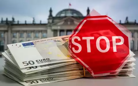 Ein Stapel Euro-Banknoten, teilweise verdeckt von einem roten Stoppschild, mit einem unscharfen Regierungsgebäude im Hintergrund. - Foto: über boerse-global.de