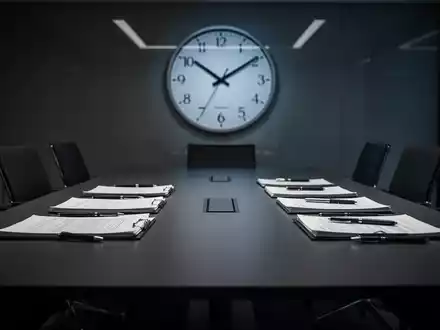 Ein Konferenztisch mit Dokumenten, der zwei streitende Parteien symbolisiert, und eine Uhr, die eine späte Stunde anzeigt. - Foto: über boerse-global.de
