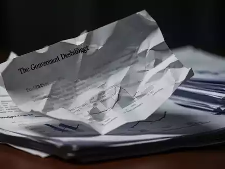 Ein zerknülltes oder gefaltetes Regierungsdokument, das geheime Sparmaßnahmen und Kürzungen symbolisiert, mit diffusem Hintergrund. - Foto: über boerse-global.de