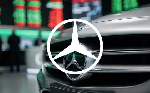 Nahaufnahme des Kühlergrills eines Mercedes-Benz mit dem Emblem, im Hintergrund verschwommen eine Börse. - Foto: über boerse-global.de