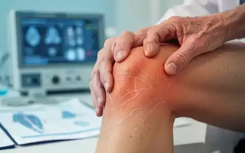 Eine Nahaufnahme einer Hand, die ein Knie berührt, symbolisiert Gelenkgesundheit und Hautalterung. Im Hintergrund verschwommene Forschungsdaten. - Foto: über boerse-global.de