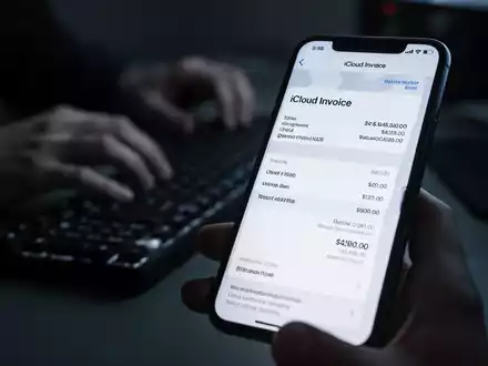 Nahaufnahme eines Smartphone-Bildschirms mit einer gefälschten iCloud-Rechnung, im Hintergrund verschwommen eine Person am Computer. - Foto: über boerse-global.de