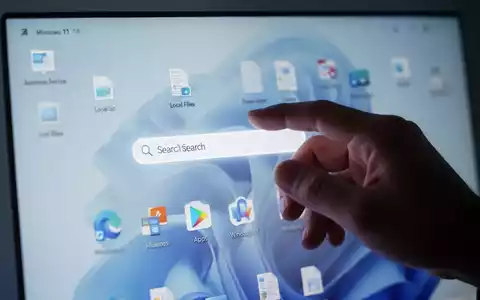 A hand interacts with a computer screen showing a Windows 11 search bar prioritizing local files and apps over web results. - Foto: über boerse-global.de