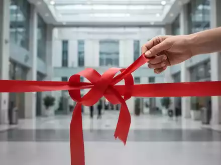Eine Hand entwirrt ein kompliziertes Knäuel aus rotem Band, vor dem unscharfen Hintergrund eines modernen Regierungsgebäudes. - Foto: über boerse-global.de