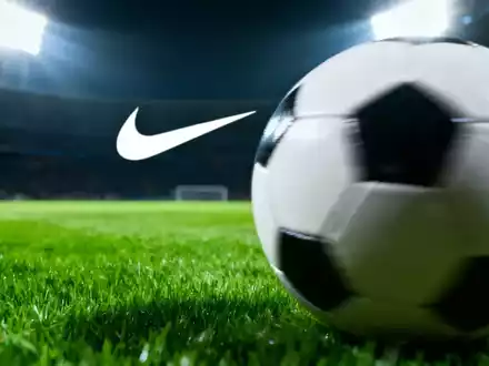 Ein unscharfer Fußball auf einem grünen Rasen mit einem angedeuteten Nike-Swoosh im Hintergrund unter Stadionlichtern. - Foto: über boerse-global.de