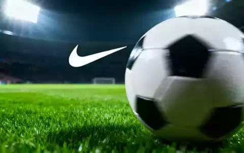 Ein unscharfer Fußball auf einem grünen Rasen mit einem angedeuteten Nike-Swoosh im Hintergrund unter Stadionlichtern. - Foto: über boerse-global.de