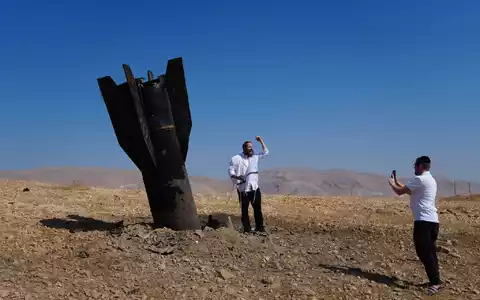 Menschen neben dem Wrack einer iranischen Rakete, die im Westjordanland eingeschlagen ist. - Foto: Mahmoud Illean/AP/dpa