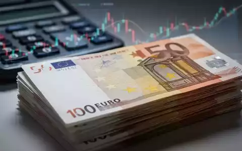 Nahaufnahme eines Stapels Euro-Banknoten, im Hintergrund verschwommen ein Taschenrechner oder Finanzdiagramm, das Löhne und Daten symbolisiert. - Foto: über boerse-global.de